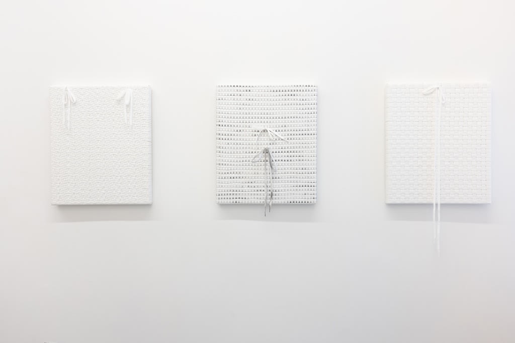 Installation of Didi Rojas exhibition - three shoelace woven paintings hanging on wall (white on white)