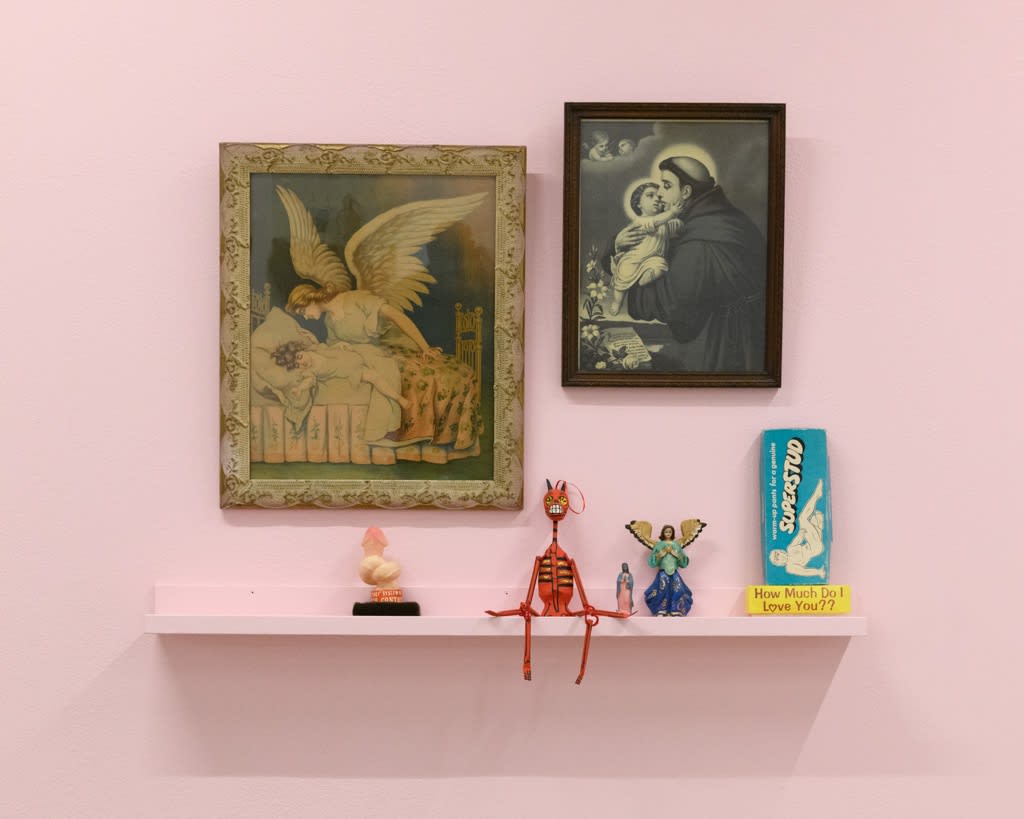 installation of Gina M. Contreras exhibition - pink wall with religious paintings and sculptural mementos from the artist