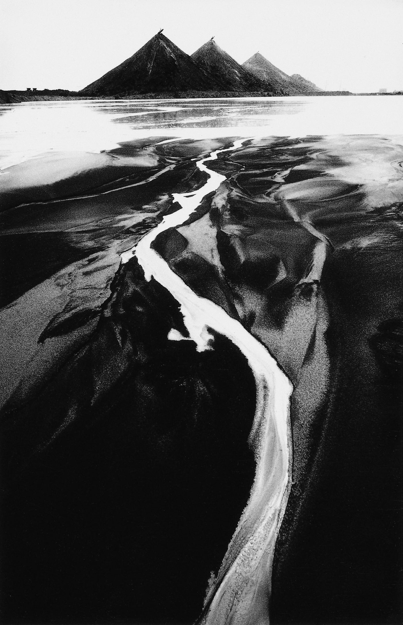 Michal Cala, Slagheap, Czeriwonka, 1978, Silesia, Poland, looking like the mountains in background and the river or a stream of water, black and white graphic landscape of a slagheap in Poland with a track path made by some small river or rain directly go