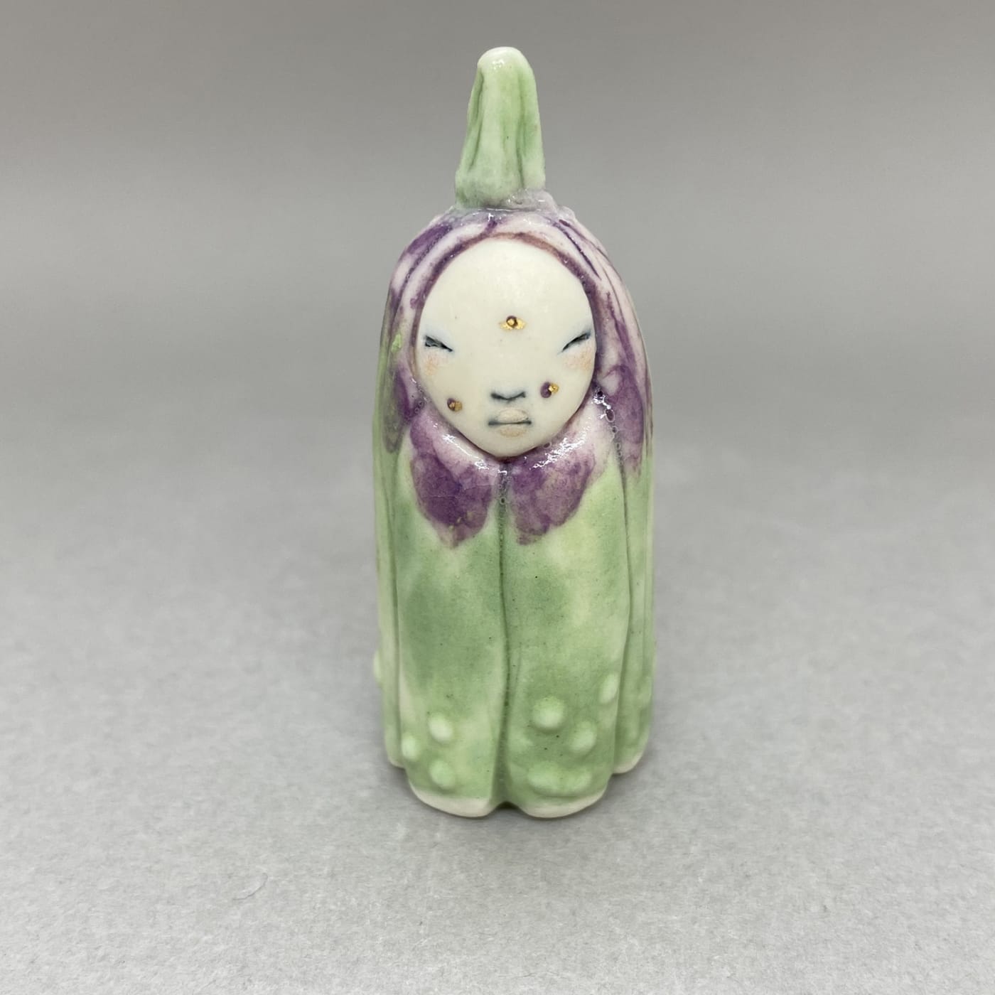 A tiny sculpture of a plant spirit in green with purple petal shapes around its face