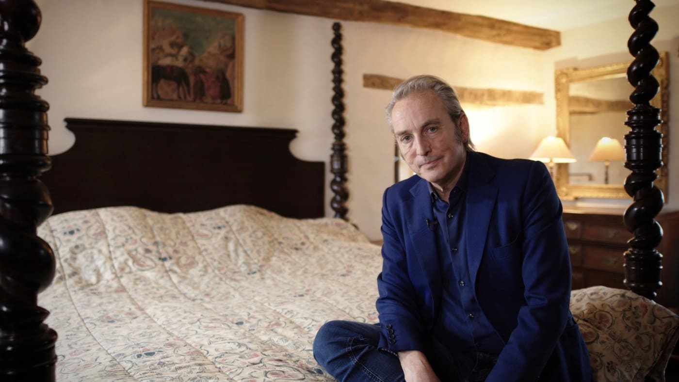 Philip Mould sitting on four poster bed in front of Roger Fry Bloomsbury painting