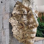 Sculpture murale contemporaine représentant un masque, en alliage avec feuille d’or et patine noire, œuvre expressive pour architecture intérieure.