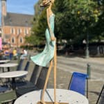 marchant sur un rêve sculpture contemporaine de femme de Hedwige Leroux fille de la ville dans un écouteur écoutant de la musique et en robe verte comme une fleur look d'été sculpture en bronze sculpture figurative à la galerie Art Yi à Bruxelles