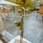 In attesa di un cartello scultura di Hedwige Leroux una ragazza scultura scultura contemporanea scultura donna contemporanea scultura in bronzo una giovane ragazza che cammina con il suo vestito verde e che chiama al telefono per aspettare un messaggio Galleria Art Yi Galleria d'arte di Bruxelles
