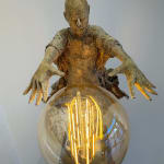 Visionary XL met lichtgevende jongen sculptuur, bronzen sculptuur van Lieven d'Haese, tuinsculptuur van een jongen die zijn armen opent om een ​​gloeilamp in zijn handen aan te steken met verbeeldingskracht, magie, droom, hedendaagse kunstsculptuur, licht, interieurontwerp in de Art Yi galerie in Brussel.