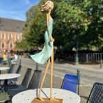 walking on a dream contemporary woman sculpture of Hedwige Leroux city girl in earphone listening to music and in green dress like a flower summer look bronze sculpture figurative sculpture at Art Yi gallery in Brussels