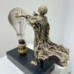 Visionary XL met lichtgevende jongen sculptuur, bronzen sculptuur van Lieven d'Haese, tuinsculptuur van een jongen die zijn armen opent om een ​​gloeilamp in zijn handen aan te steken met verbeeldingskracht, magie, droom, hedendaagse kunstsculptuur, licht, interieurontwerp in de Art Yi galerie in Brussel.