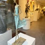 In attesa di un cartello scultura di Hedwige Leroux una ragazza scultura scultura contemporanea scultura donna contemporanea scultura in bronzo una giovane ragazza che cammina con il suo vestito verde e che chiama al telefono per aspettare un messaggio Galleria Art Yi Galleria d'arte di Bruxelles