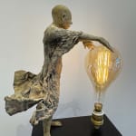 Visionary XL met lichtgevende jongen sculptuur, bronzen sculptuur van Lieven d'Haese, tuinsculptuur van een jongen die zijn armen opent om een ​​gloeilamp in zijn handen aan te steken met verbeeldingskracht, magie, droom, hedendaagse kunstsculptuur, licht, interieurontwerp in de Art Yi galerie in Brussel.