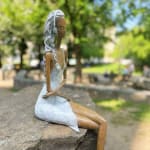 Stand by me vrouw sculptuur Hedwige Leroux hedendaagse kunst hedendaagse sculptuur interieurontwerp een sculptuur van een jong stadsmeisje dat in jeans ligt en naar muziek luistert een meisje dat zit en met haar koptelefoon naar muziek luistert Galerie Art Yi Brussels Art Gallery