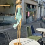 marchant sur un rêve sculpture contemporaine de femme de Hedwige Leroux fille de la ville dans un écouteur écoutant de la musique et en robe verte comme une fleur look d'été sculpture en bronze sculpture figurative à la galerie Art Yi à Bruxelles