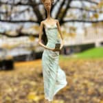 In attesa di un cartello scultura di Hedwige Leroux una ragazza scultura scultura contemporanea scultura donna contemporanea scultura in bronzo una giovane ragazza che cammina con il suo vestito verde e che chiama al telefono per aspettare un messaggio Galleria Art Yi Galleria d'arte di Bruxelles