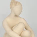 Seated white ceramic figure is looking over her left shoulder with arms draped around her knees which are tucked together.