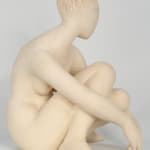 Seated white ceramic figure is looking over her left shoulder with arms draped around her knees which are tucked together.