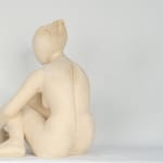 Seated white ceramic figure is looking over her left shoulder with arms draped around her knees which are tucked together.