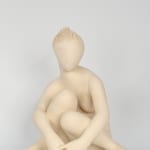 Seated white ceramic figure is looking over her left shoulder with arms draped around her knees which are tucked together.