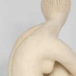 Seated white ceramic figure is looking over her left shoulder with arms draped around her knees which are tucked together.