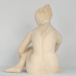 Seated white ceramic figure is looking over her left shoulder with arms draped around her knees which are tucked together.