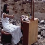 Artist Chen Qiulin in modern white skirt sits in front of a dressing table located on the ruins.