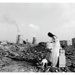 A fair maiden in white long skirt is putting on makeup and behind her and her dressing table, there are two industrial chimneys in the background