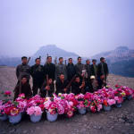A group of Bang Bang men stand in two rows with vases of flowers in front of them.