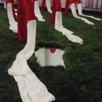 Chen Qiulin's installation work that is composed of red and white long peking opera sleeves with artificial arms; these sleeves are placed indoor on a man-made lawn; a mirror is also placed on this lawn.