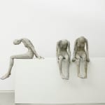 Three women sit on a white table with their heads bent.