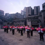 A group of Bang Bang men holding flowers stand on the ground and behind them are the old residential communities.