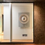 Silver-toned kinetic wall sculpture by Damien Bénéteau featuring a central rotating disc inside a circular form, lit with integrated LED light on an anodised aluminium panel.