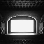 Black-and-white photograph of an empty ornate with a glowing white screen onstage