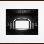 Framed black-and-white photograph of an empty ornate with a glowing white screen onstage