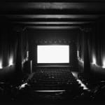 Black-and-white photograph of a mostly-empty movie theater with a blank glowing white screen