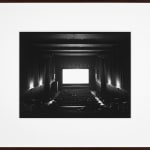 Framed black-and-white photograph of a mostly-empty movie theater with a blank glowing white screen