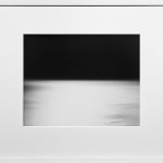 Framed black-and-white photograph of an out-of-focus shimmery seascape across the lower half against the pitch dark sky above