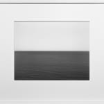 Framed black-and-white photograph of a calm dark gray seascape across the lower half with a blank light gray sky above