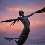 A monumental bronze sculpture of a winged female by Nicola Godden stands in front of a sunset at a Dorset sculpture park, Sculpture by the Lakes