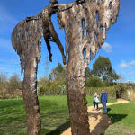 Two people are looking up at a monumental bronze sculpture of a mythological figure at a Dorset sculpture park.