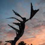 A monumental bronze sculpture of a winged female by Nicola Godden stands in front of a sunset at a Dorset sculpture park, Sculpture by the Lakes