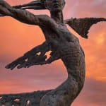 A monumental bronze sculpture of a winged female by Nicola Godden stands in front of a sunset at a Dorset sculpture park, Sculpture by the Lakes, close up of figure