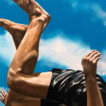Man in bathing suit doing a cannon ball dive through the air above water