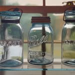 Painting of three glass ball jars sitting on a glass shelf in front of a window