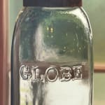 Painting of three glass ball jars sitting on a glass shelf in front of a window