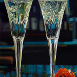 Two Crystal Champagne Glasses filled with bubbly and accompanied by a red rose.