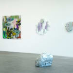 photo of a silver rock laid in a gallery space with 3 paintings on the wall