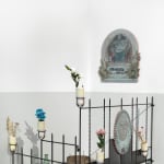 image of a mixed media installation in a sort of tomb shrine setup, consisting of fencing, flowers in containers, and two painted panels