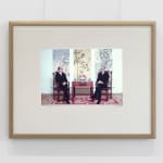 A framed image of two men sitting next to one another wearing identical suits.