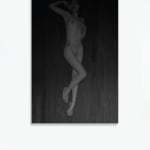 A black and white inkjet print of a nude woman lounging on a wooden floor.