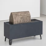 a cast iron box that has four small legs elevating it like a table, with a rounded bronze figure that comes to a point sitting on top of it.