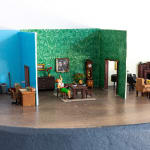 miniature diorama by Abigail Goldman of a house interior with a woman sitting at a dining table with a severed head