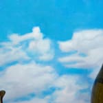 Installation featuring two bottles of wine with dog faces, two sandwiches with dog faces, a picnic basket with a baguette, an apple and a pear all with dog faces on top of a red and white checkered table clothe and a painted sky with clouds in the shape of dogs.